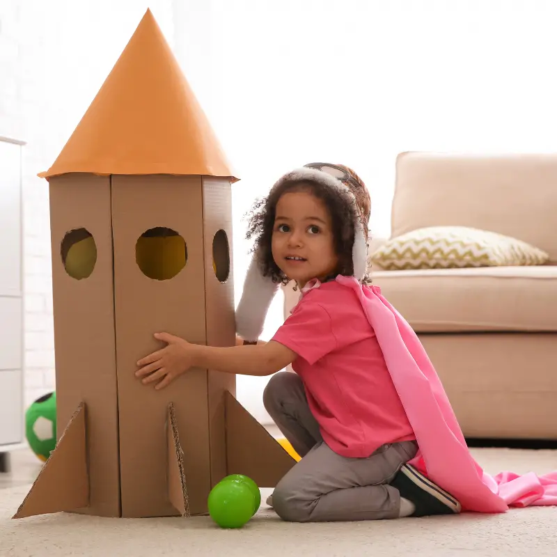 Girl playing with dress ups and cardboard space rocket