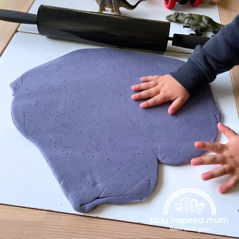 rolling out play dough to stamp dinosaur footprints